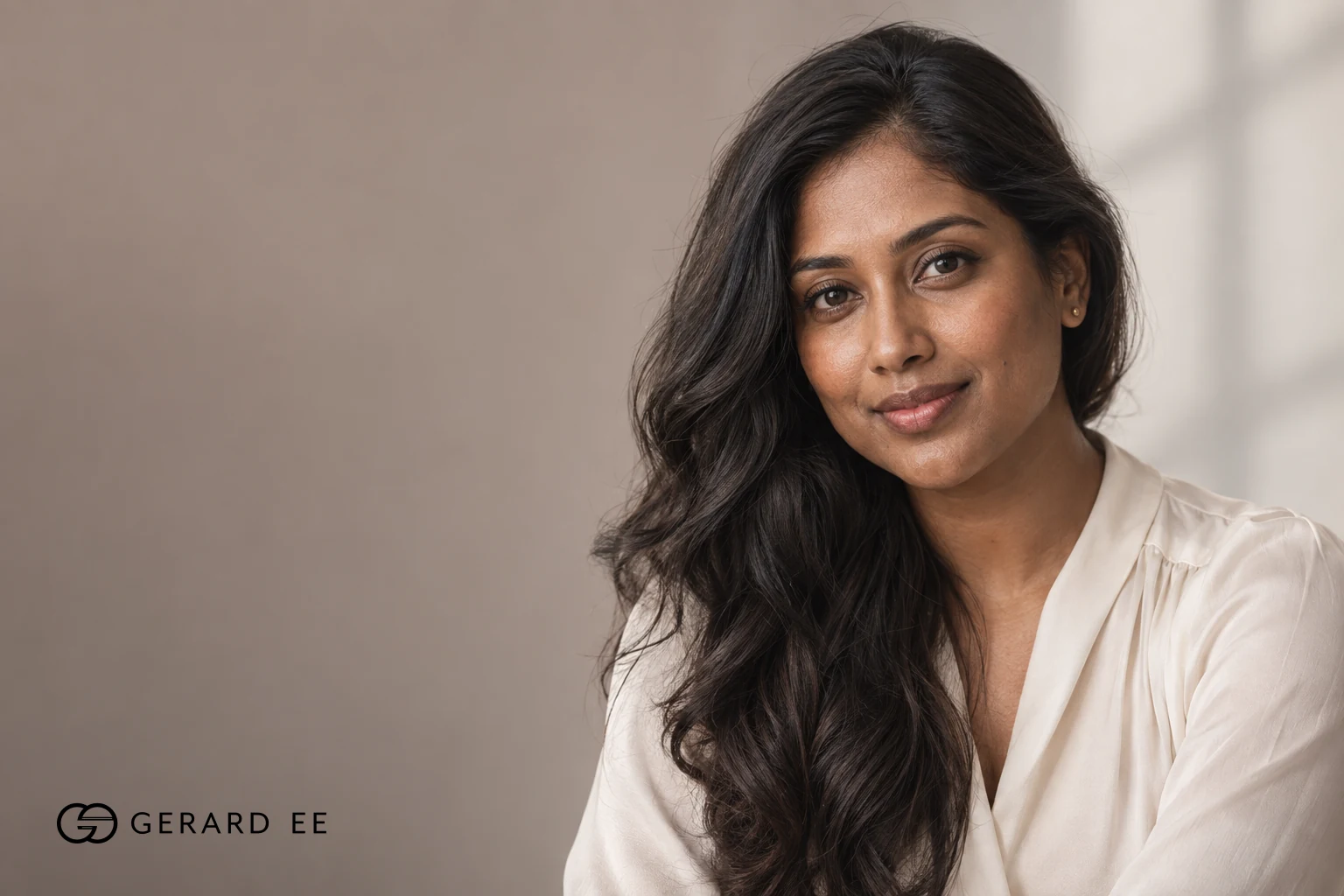 Woman with long dark hair in a cream blouse, photographed in soft natural light